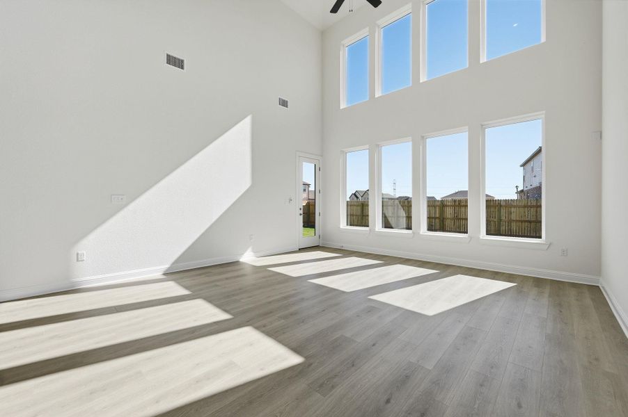 Unfurnished living room featuring light wood finished floors, ceiling fan, and a towering ceiling