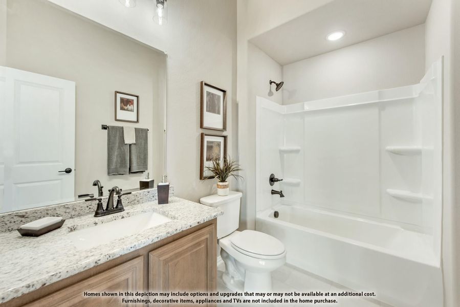 Bathroom with granite countertop vanity, wood cabinets, toilet, and white tub-shower combo