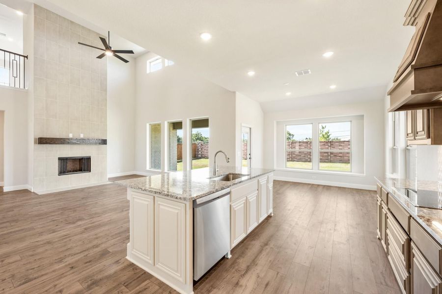 Open kitchen with granite island, white cabinets, and hardwood floors, open to living room with tall tiled fireplace