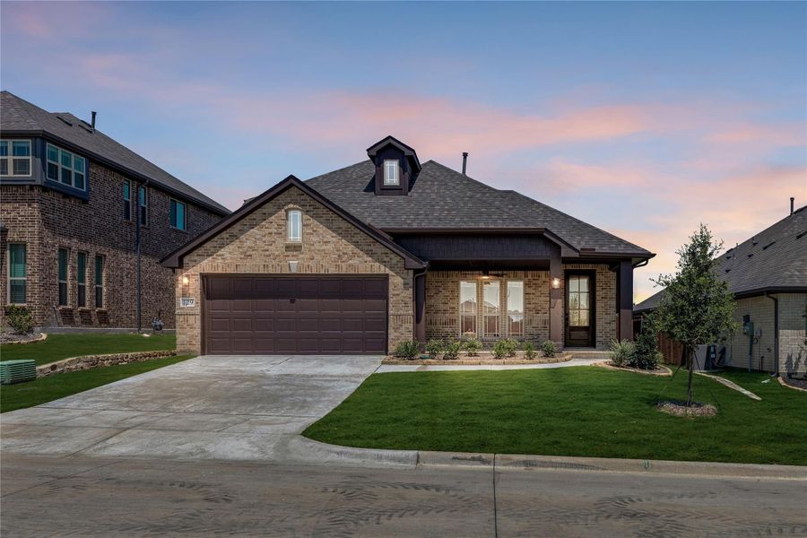 Single-story brick home with two-car garage, covered entry, and manicured front lawn at dusk Single-story brick home with two-car garage, covered entry, and manicured front lawn at dusk