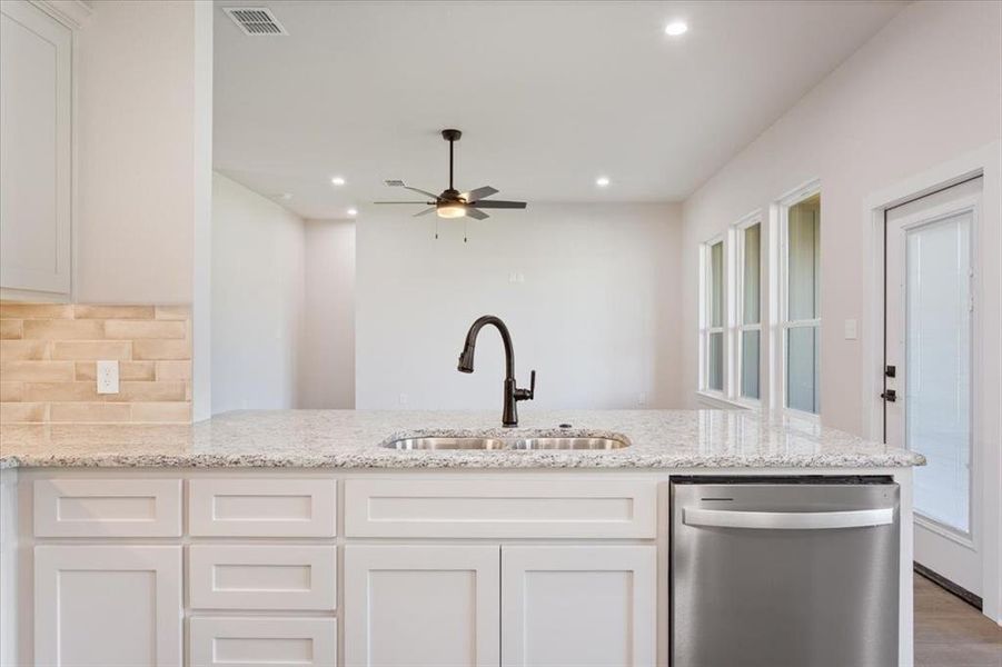 Kitchen featuring dishwasher, light stone countertops, a peninsula, white cabinetry, and a ceiling fan Kitchen featuring dishwasher, light stone countertops, a peninsula, white cabinetry, and a ceiling fan