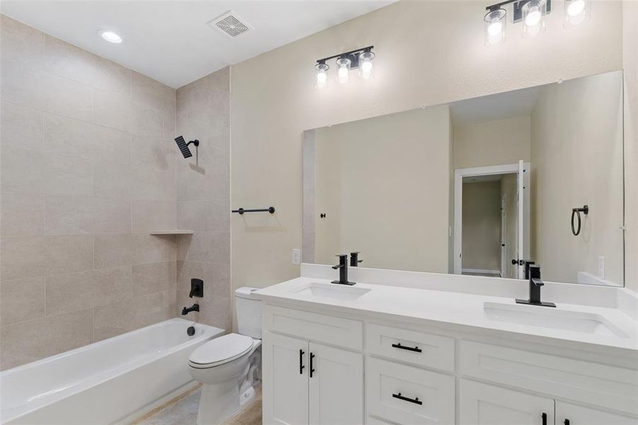 Full bathroom featuring vanity, tiled shower / bath combo, and toilet