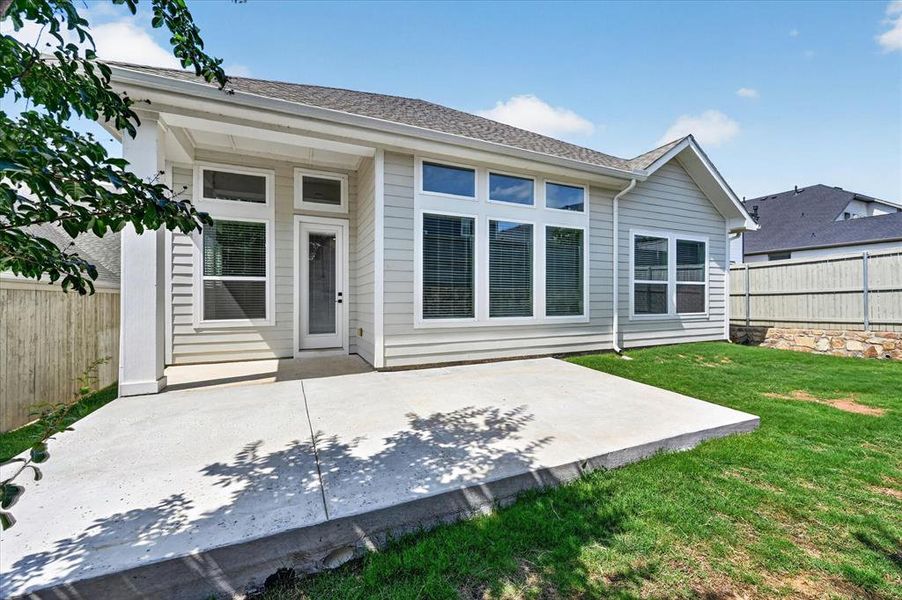Rear exterior featuring a spacious concrete patio, light-colored horizontal siding, multiple large windows, a screened door, and a grass lawn Rear exterior featuring a spacious concrete patio, light-colored horizontal siding, multiple large windows, a screened door, and a grass lawn