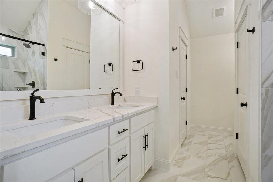 Bathroom with light marble finish flooring, a marble finish shower, and double vanity