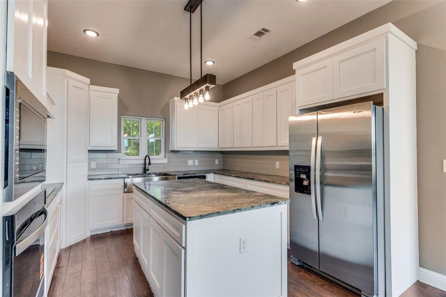 Kitchen featuring stainless steel appliances, decorative backsplash, dark wood-style flooring, dark stone countertops, and white cabinets Kitchen featuring stainless steel appliances, decorative backsplash, dark wood-style flooring, dark stone countertops, and white cabinets