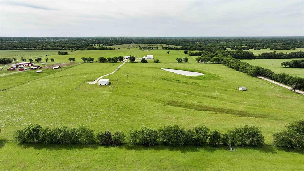 Expansive green acreage featuring multiple outbuildings, a private pond, and a winding driveway