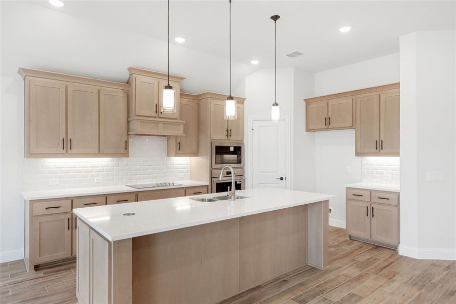 Kitchen with large island, light wood cabinets, white countertops, and pendant lights over sink