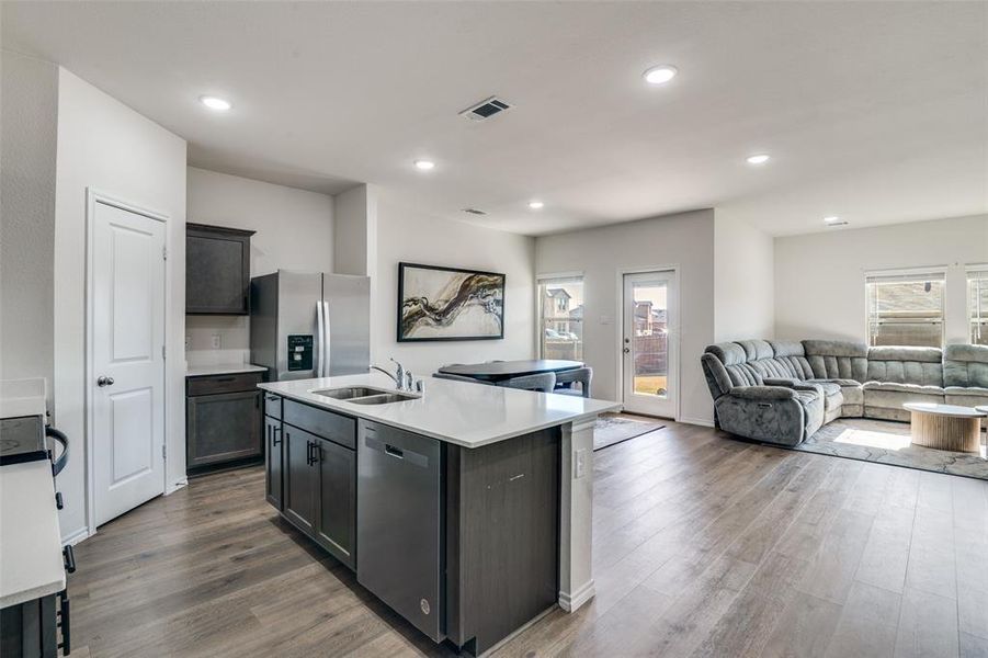 Kitchen featuring a center island with sink, open floor plan, stainless steel appliances, dark wood finished floors, and light stone counters Kitchen featuring a center island with sink, open floor plan, stainless steel appliances, dark wood finished floors, and light stone counters