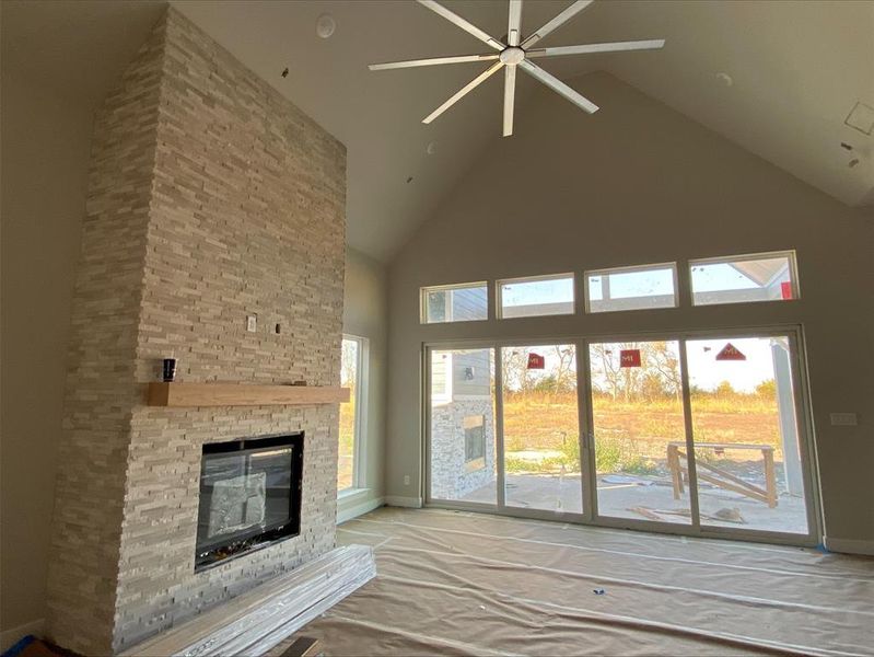 Unfurnished living room featuring high vaulted ceiling, a ceiling fan, and a fireplace Unfurnished living room featuring high vaulted ceiling, a ceiling fan, and a fireplace