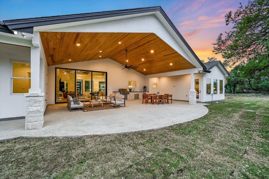 Back of house at dusk featuring stucco siding, an outdoor kitchen / dining area, a ceiling fan, a patio, and a yard