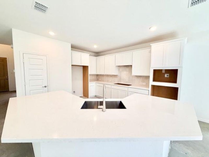 Kitchen with white cabinets, a large island with sink, recessed lighting, tasteful backsplash, and light stone counters