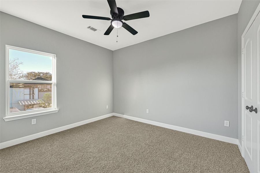 This room features soft gray walls, a plush carpet, and a ceiling fan. A window provides natural light, and there's a closet with double doors, offering a cozy and functional space.