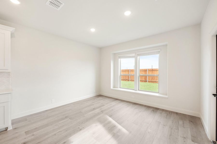 Empty room with light gray hardwood floors, white walls, and a large window overlooking a fenced backyard. Empty room with light gray hardwood floors, white walls, and a large window overlooking a fenced backyard.