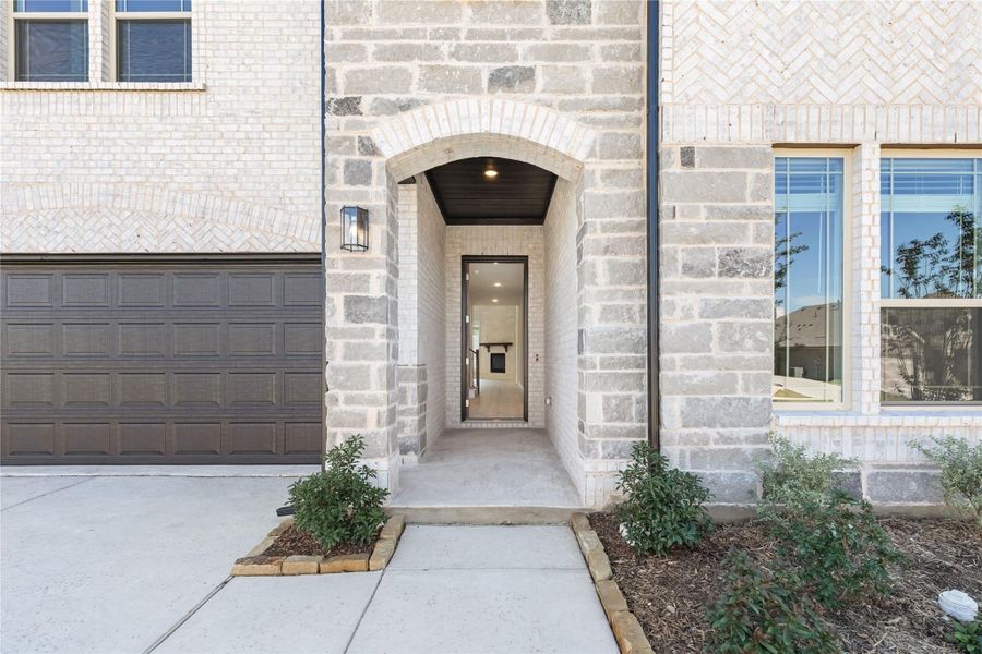 Stone brick home entrance with arched doorway, dark wood ceiling, and two-car garage nearby