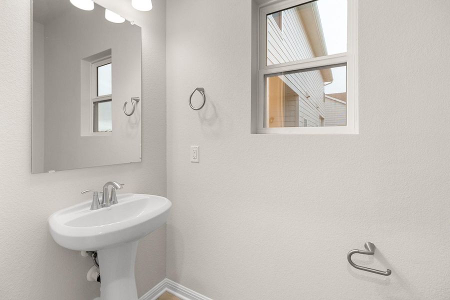 The bathroom features a white pedestal sink with a chrome faucet, a rectangular mirror, and a window providing natural light