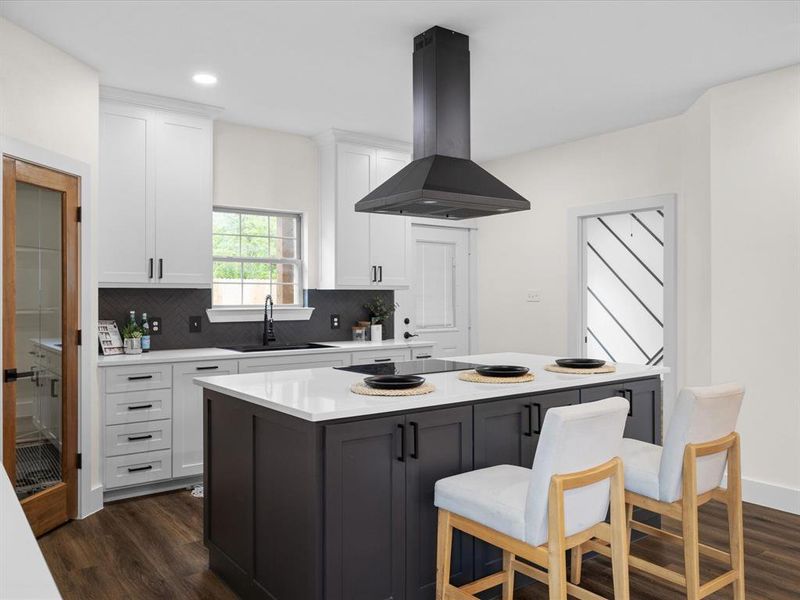 Two tone kitchen featuring two tone cabinetry, dark wood-style floors, extractor fan, a breakfast bar area, and light stone counters