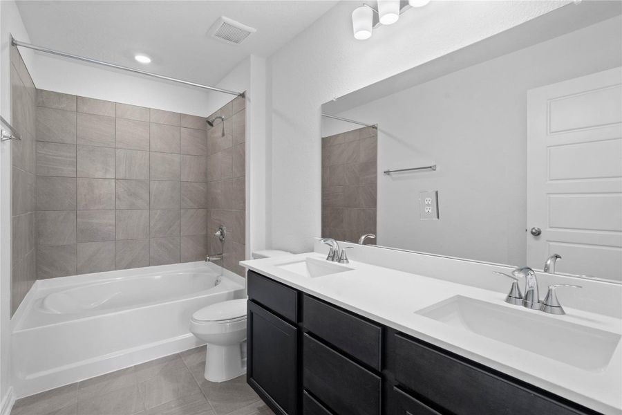 This move-in ready primary bathroom offers a spacious tub/shower combination with a tile surround, stained cabinetry topped with light countertops, dual sinks, high ceilings, neutral paint, a large mirror, and sleek, modern finishes for a polished look.