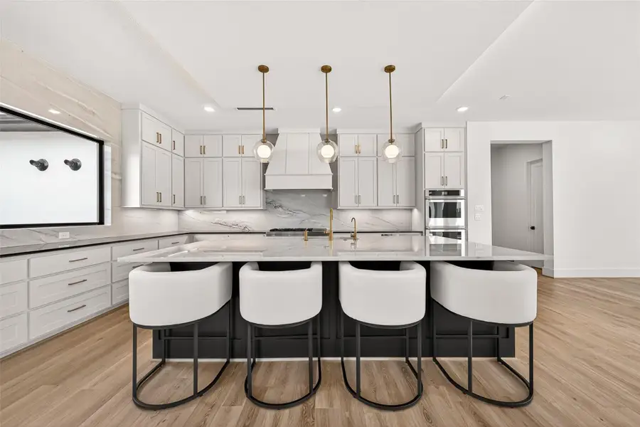 This fabulous kitchen was designed for both luxury and functionality. Anchored by an expansive quartzite island with seating for four, an undermount sink, and water filtration system, the space is enhanced by elegant pendant lighting, hidden LED ceiling accents, recessed lighting, and striking black-and-white contrasting cabinetry with gold hardware.