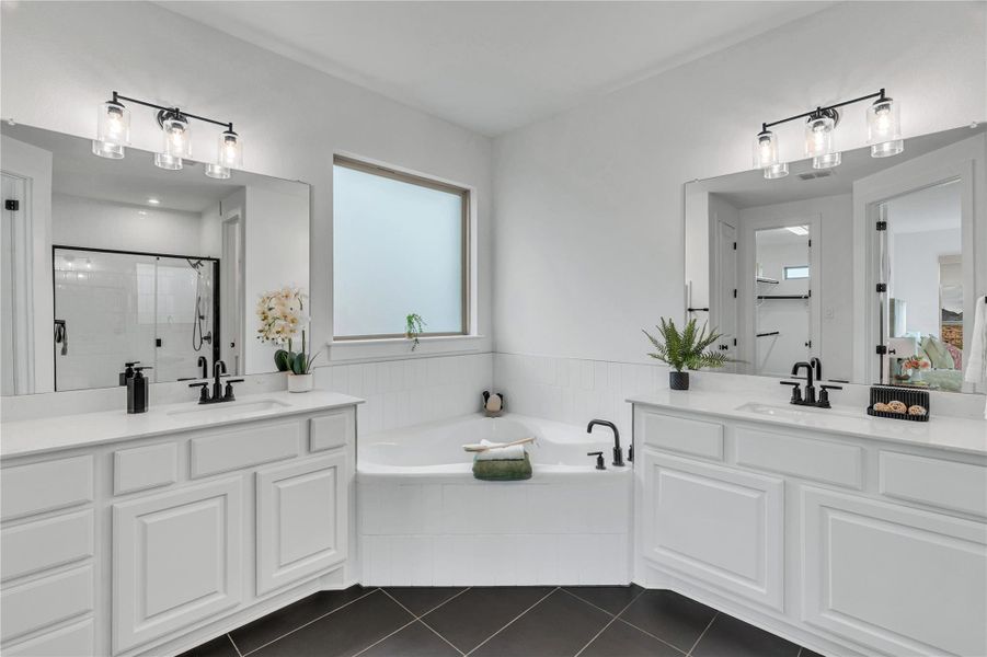 A corner soaking tub centers this bathroom with dual vanities and modern tile flooring.