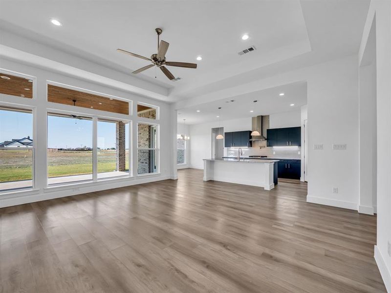 Unfurnished living room with a raised ceiling, ceiling fan with notable chandelier, and dark hardwood / wood-style flooring