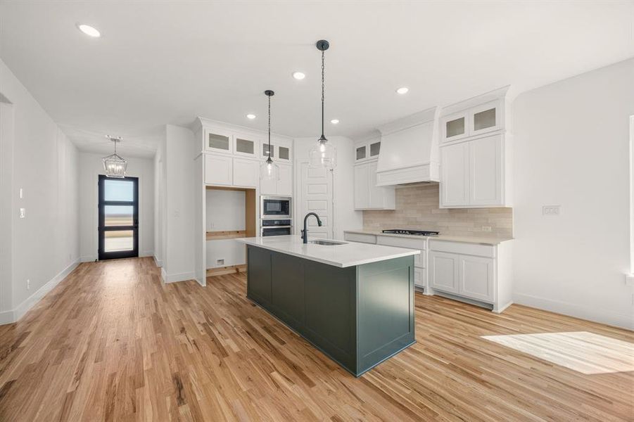 Dual tone kitchen featuring dual tone cabinets, a center island with sink, light wood finished floors, built in microwave, and glass insert cabinets