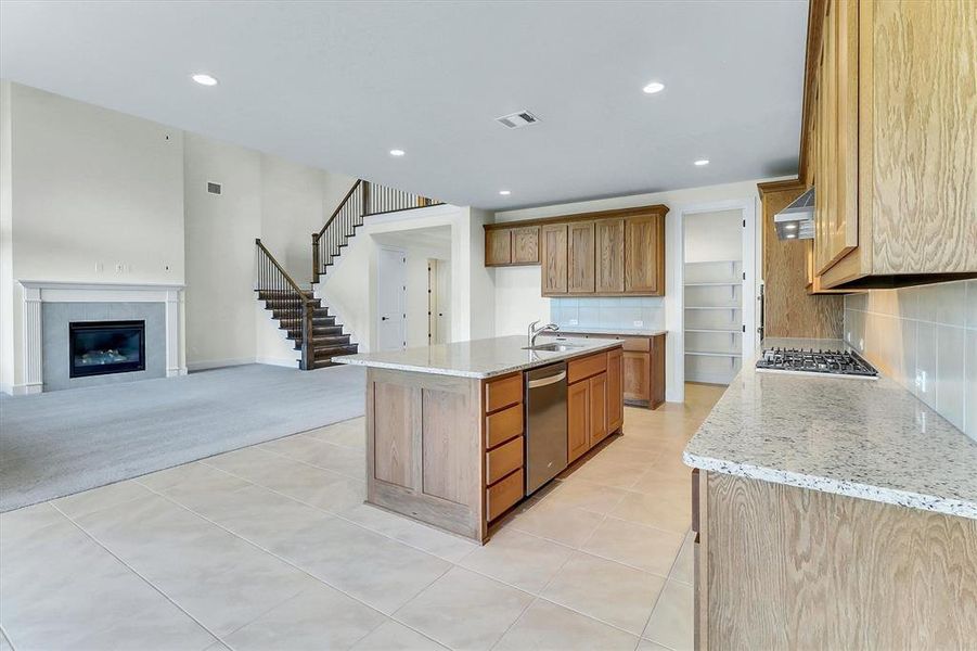 Open-concept living space featuring a central kitchen island with a stainless steel dishwasher, wood-finish cabinetry, speckled countertops, and a gas cooktop Open-concept living space featuring a central kitchen island with a stainless steel dishwasher, wood-finish cabinetry, speckled countertops, and a gas cooktop