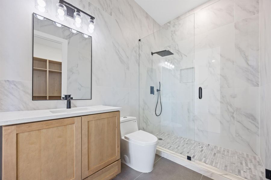 Bathroom with vanity, a marble finish shower, tile walls, and dark tile patterned floors