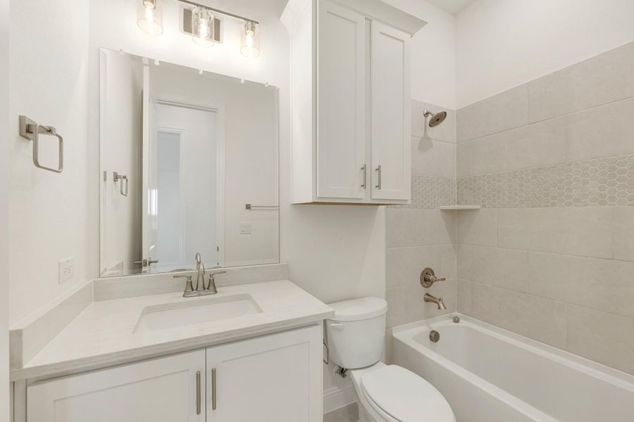 Bathroom with white vanity, quartz countertop, tub-shower combo with beige tile, and upper storage cabinet