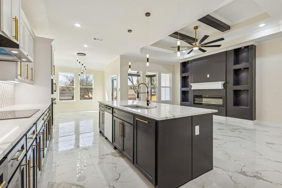 Kitchen featuring pendant lighting, ornamental molding, open floor plan, an island with sink, and light stone countertops