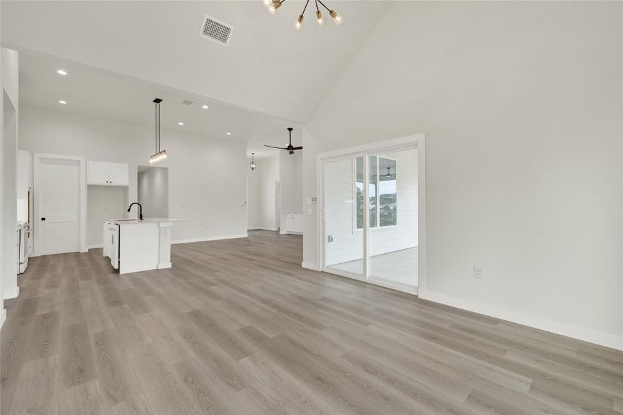 Unfurnished living room with high vaulted ceiling, a chandelier, light wood-style floors, a ceiling fan, and recessed lighting