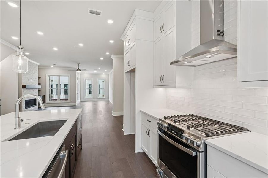 Dual tone kitchen with stainless steel appliances, light stone counters, a large fireplace, decorative light fixtures, and dark wood finished floors