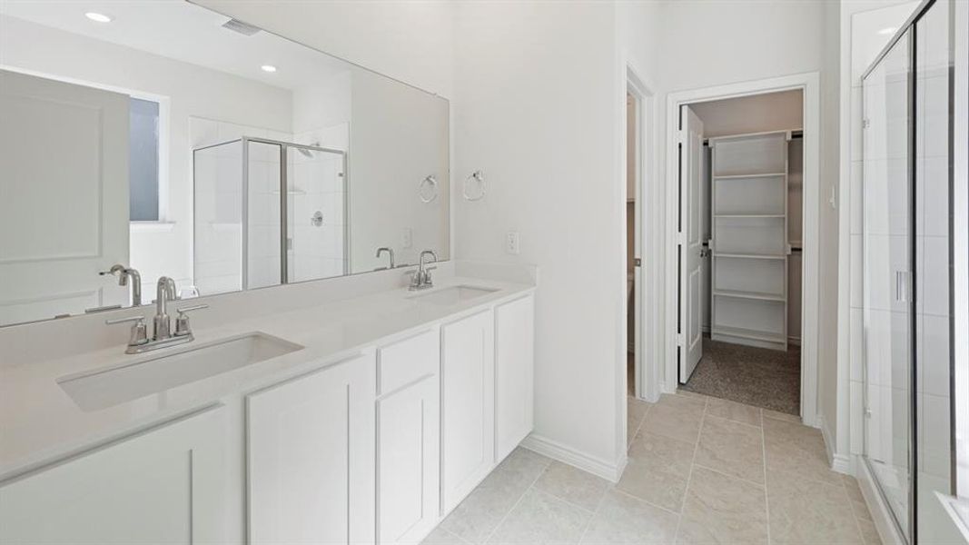 Full bathroom with a stall shower, double vanity, a walk in closet, and light tile patterned floors Full bathroom with a stall shower, double vanity, a walk in closet, and light tile patterned floors