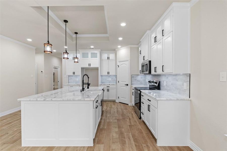 Kitchen with white cabinets, decorative light fixtures, stainless steel appliances, and a kitchen island with sink