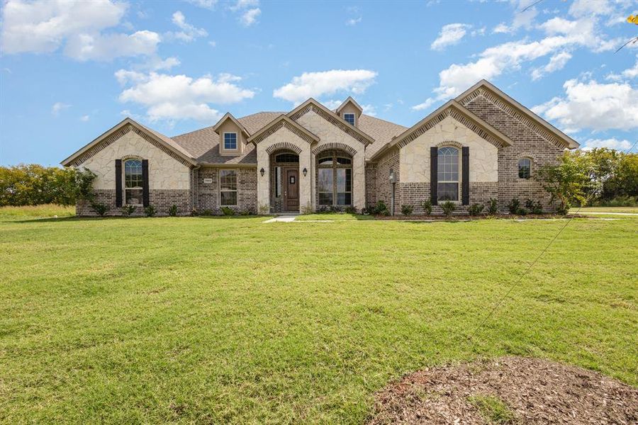 French country inspired facade featuring stone siding, brick siding, a front lawn, and roof with shingles French country inspired facade featuring stone siding, brick siding, a front lawn, and roof with shingles
