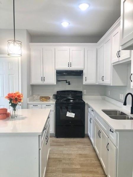 Kitchen featuring extractor fan, light wood-type flooring, black electric range, sink, and white cabinets