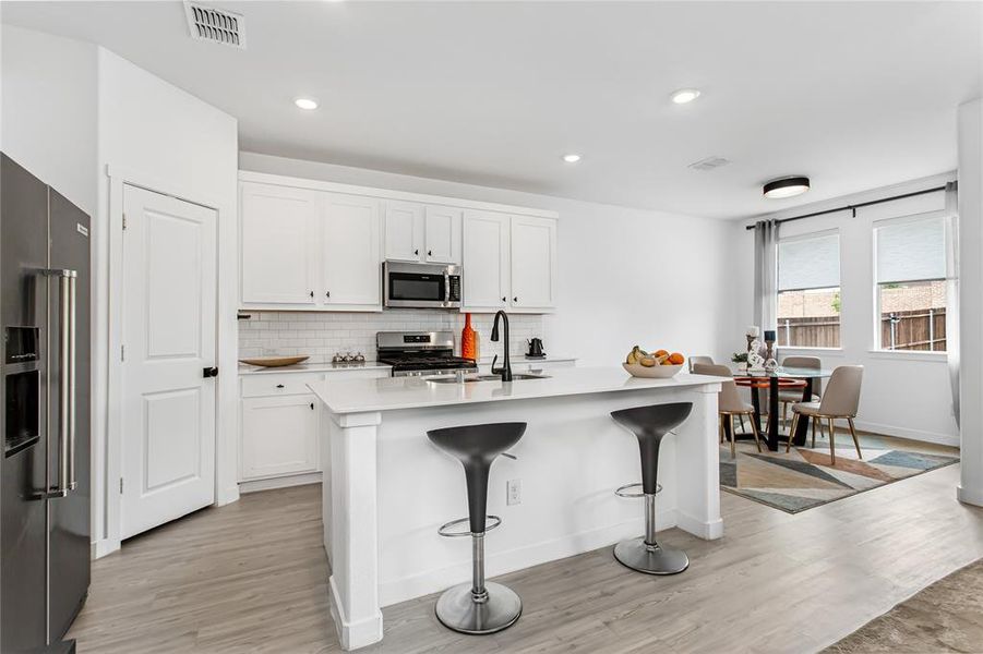 The kitchen features white cabinetry, a kitchen island with seating, stainless steel appliances, and wood-look flooring
