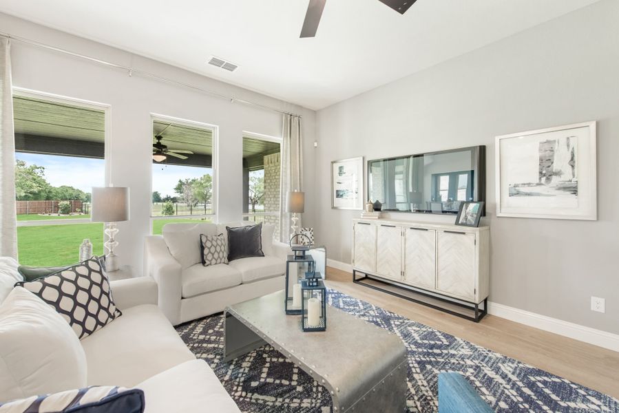 Living room with white sofas, large windows, ceiling fan, and TV on a white sideboard with hardwood floors