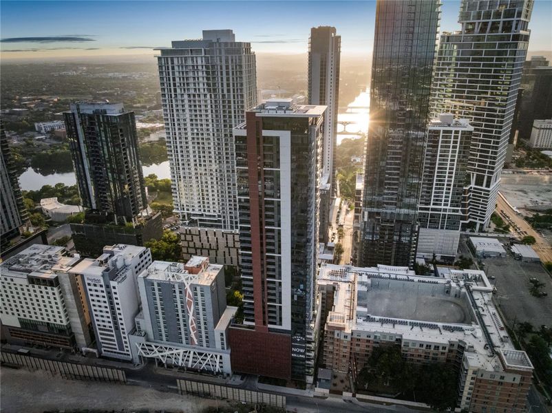 A dynamic aerial view of a vibrant urban landscape at sunset, showcasing modern high-rises and a reflective waterway.