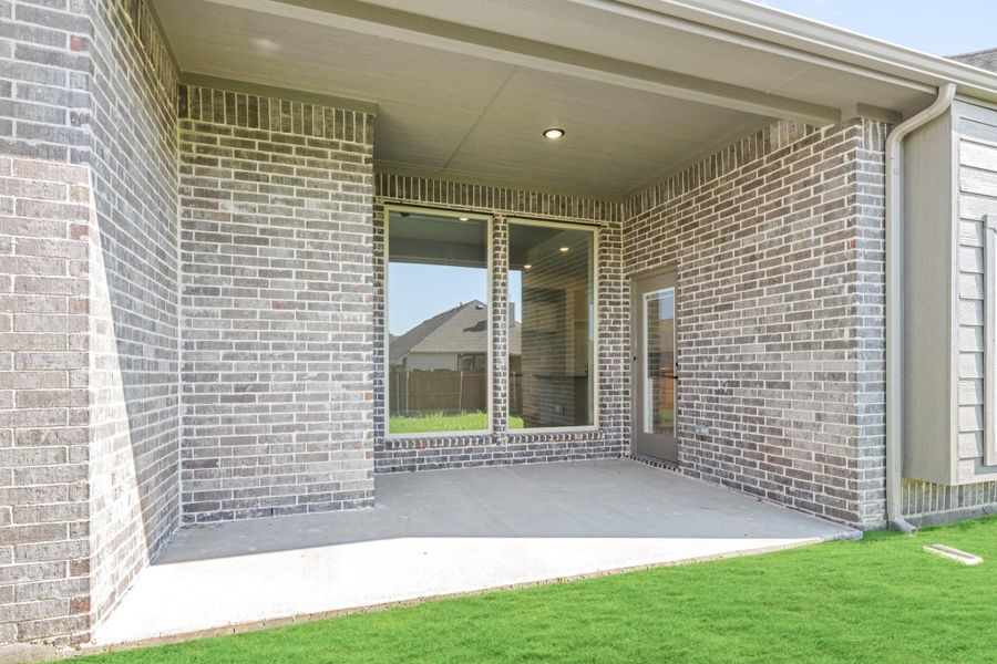 Covered back patio with concrete floor, brick walls, large window, and back door entry Covered back patio with concrete floor, brick walls, large window, and back door entry