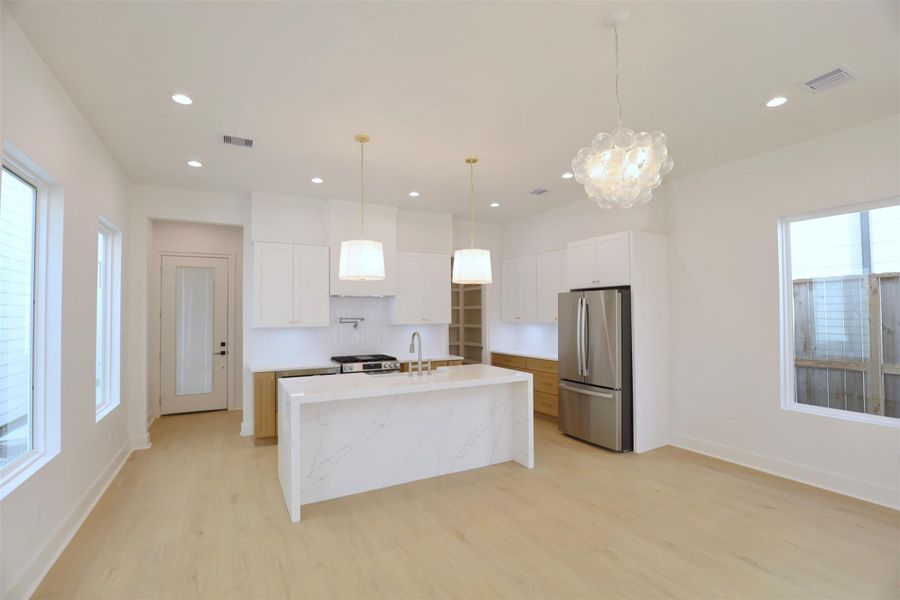Dining room flows seamlessly from the kitchen, with windows on either side that fill the space with natural light, complemented by a glass bubble chandelier overhead. Dining room flows seamlessly from the kitchen, with windows on either side that fill the space with natural light, complemented by a glass bubble chandelier overhead.
