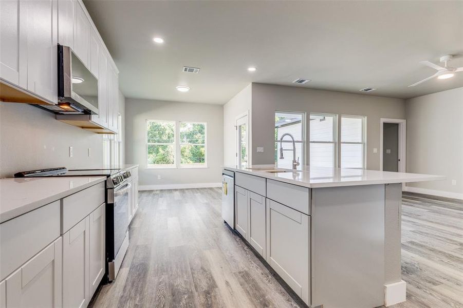 Kitchen with light hardwood / wood-style flooring, appliances with stainless steel finishes, an island with sink, sink, and ceiling fan