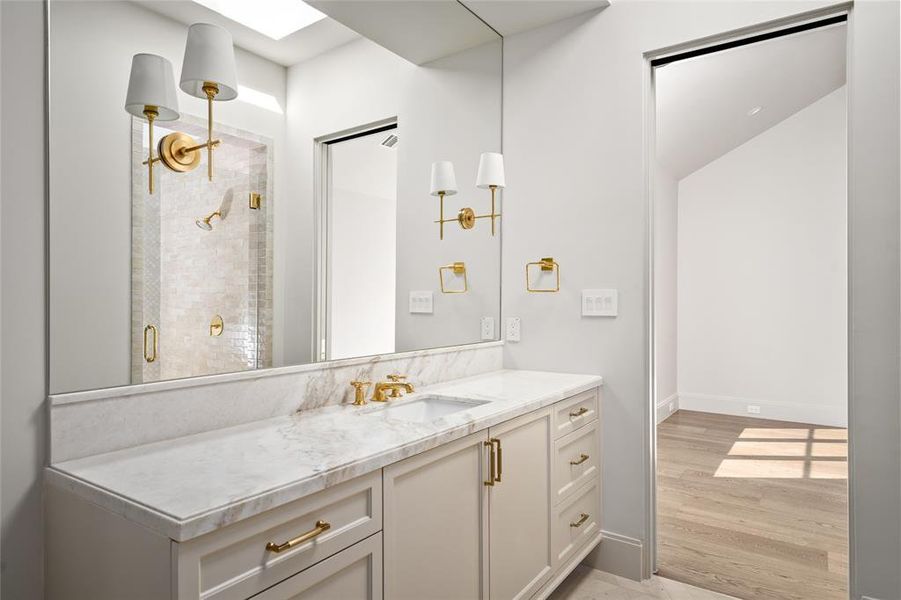 This ensuite bathroom is a sophisticated retreat, featuring a Calacatta marble vanity with elegant Top Knobs hardware. A skylight fills the space with natural light, enhancing the refined ambiance. Thomas O’Brien sconces add a touch of designer charm, while the glass-entry walk-in shower showcases Tribeca subway tile walls for a timeless, spa-like experience.