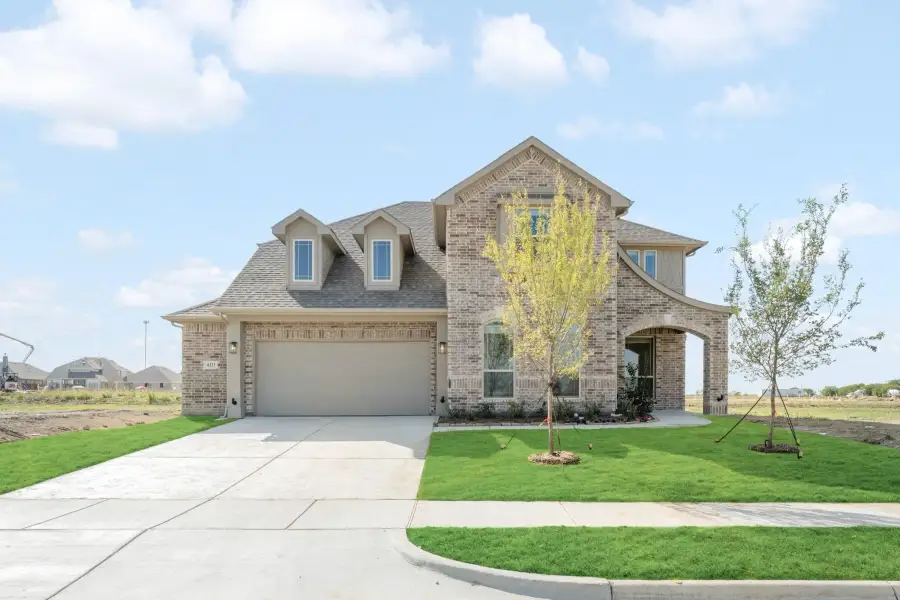 Two-story brick home with two-car garage, arched entry, dormers, and freshly landscaped front yard