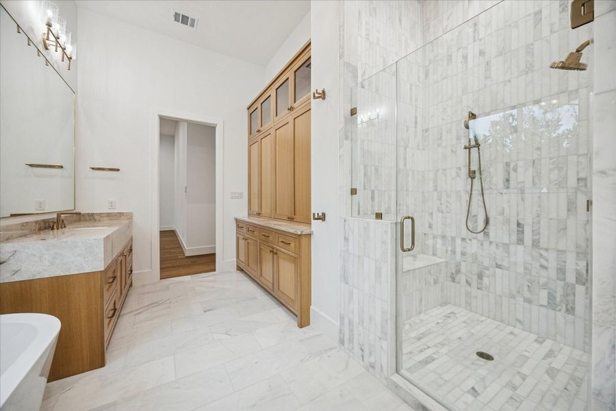 Natural stone, custom white oak cabinetry, 12 ft ceilings, and a dual-fixture glass shower define the space. Spray foam insulation and Pella windows support quiet, energy-efficient luxury.
