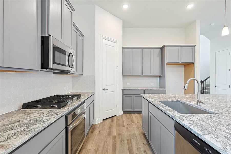 Kitchen with stainless steel appliances, sink, light stone countertops, pendant lighting, and light hardwood / wood-style floors