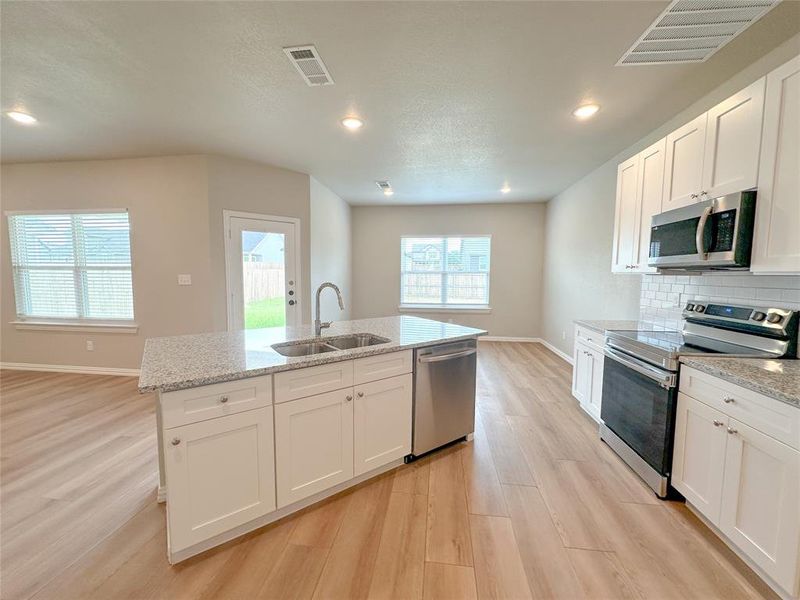 Kitchen featuring backsplash, sink, light wood-type flooring, stainless steel appliances, and white cabinets