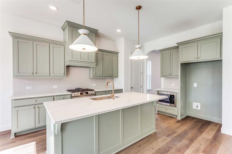 Kitchen featuring light stone countertops, appliances with stainless steel finishes, sink, wood-type flooring, and pendant lighting