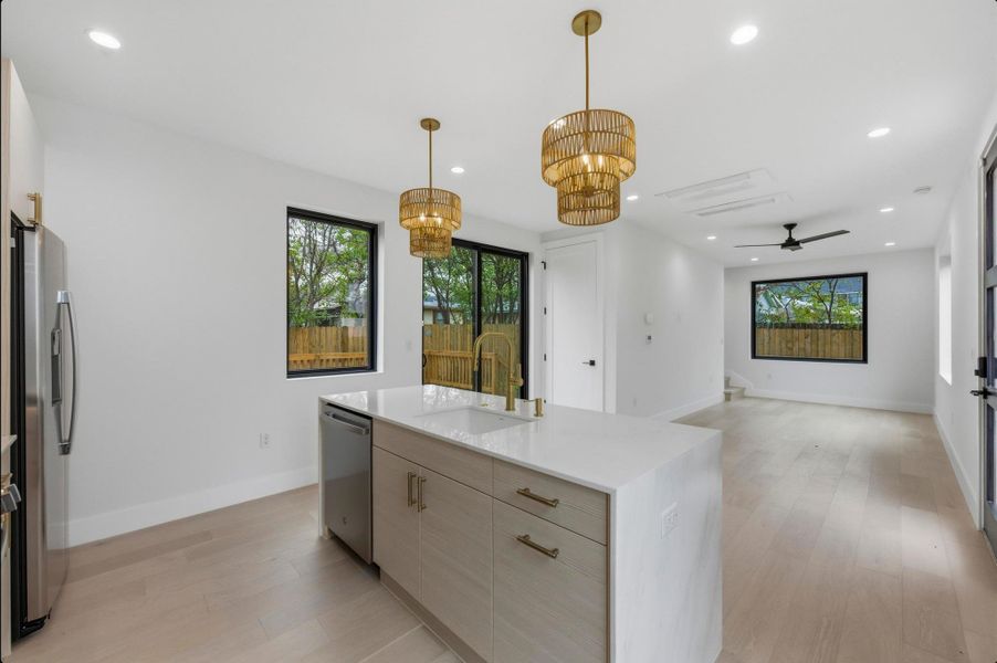Kitchen featuring light brown cabinetry, open floor plan, light wood finished floors, light stone countertops, and decorative light fixtures Kitchen featuring light brown cabinetry, open floor plan, light wood finished floors, light stone countertops, and decorative light fixtures
