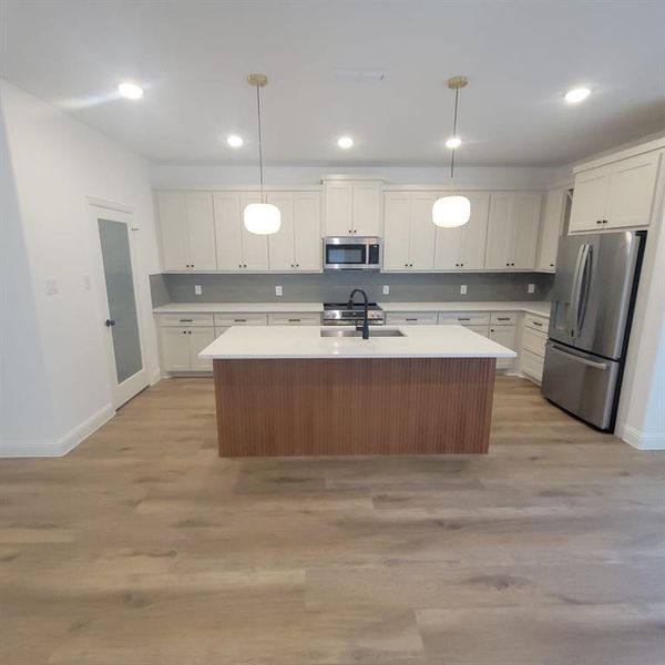 Kitchen with light hardwood / wood-style floors, white cabinets, decorative light fixtures, and appliances with stainless steel finishes