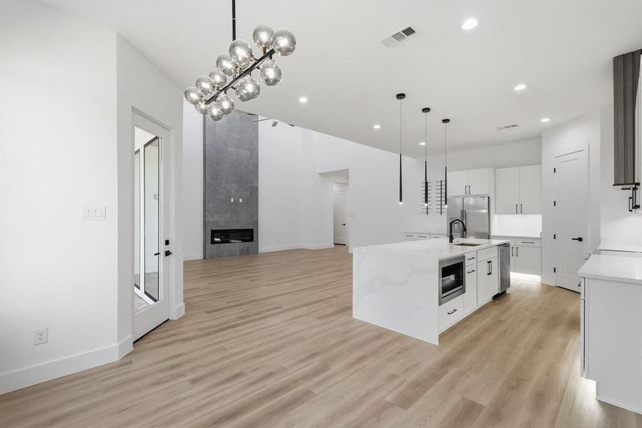 Kitchen featuring hanging light fixtures, white cabinetry, light stone counters, open floor plan, and light wood-style floors Kitchen featuring hanging light fixtures, white cabinetry, light stone counters, open floor plan, and light wood-style floors